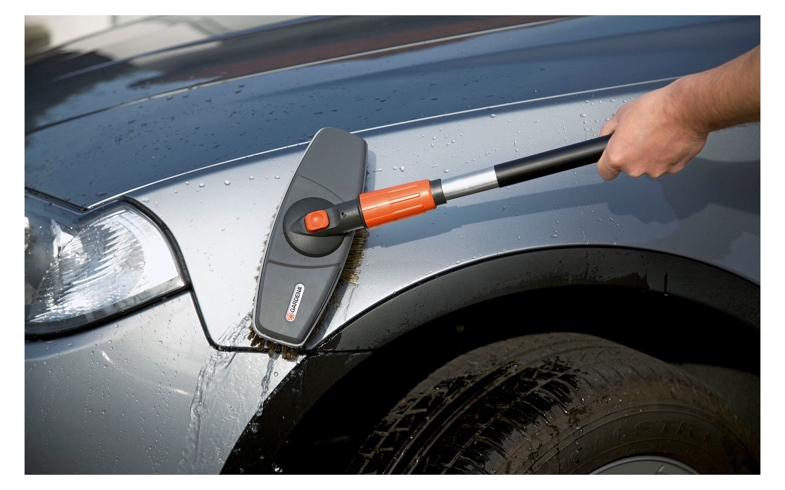 Hand holding a cleaning device on the side of a gray car