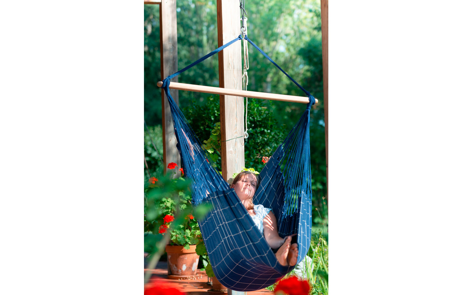 Kind liegt in einer Hängematte in einem Raum mit großen Fenstern und Pflanzen