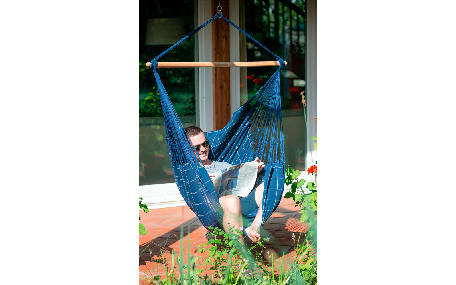 Mann sitzt in einer blauen Hängematte vor einem Haus