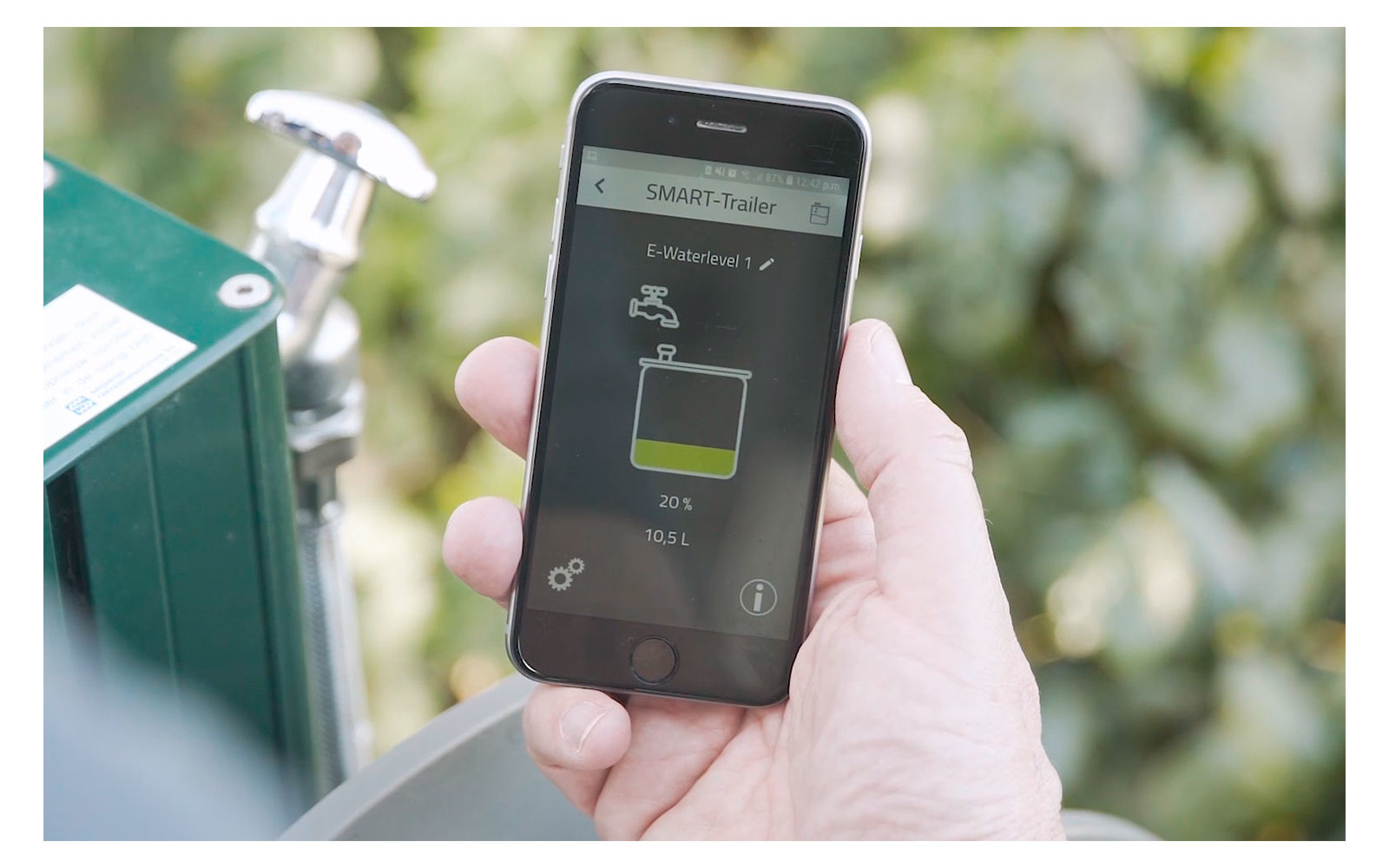Hand hält Smartphone mit App, die Akku-Ladestatus anzeigt, im Hintergrund Ladestation