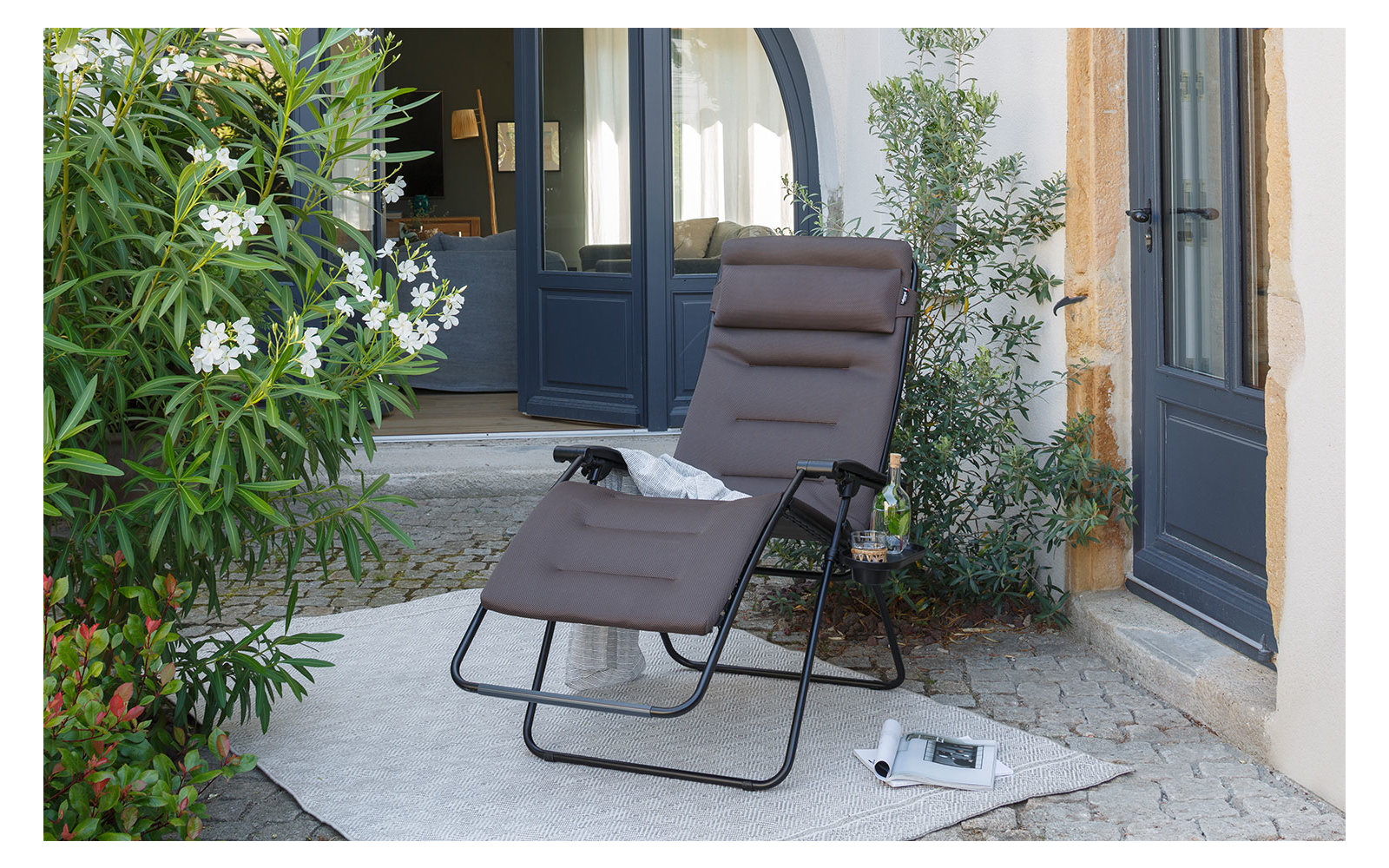 Moderne grijze fauteuil op een terras naast een houten tafel en planten