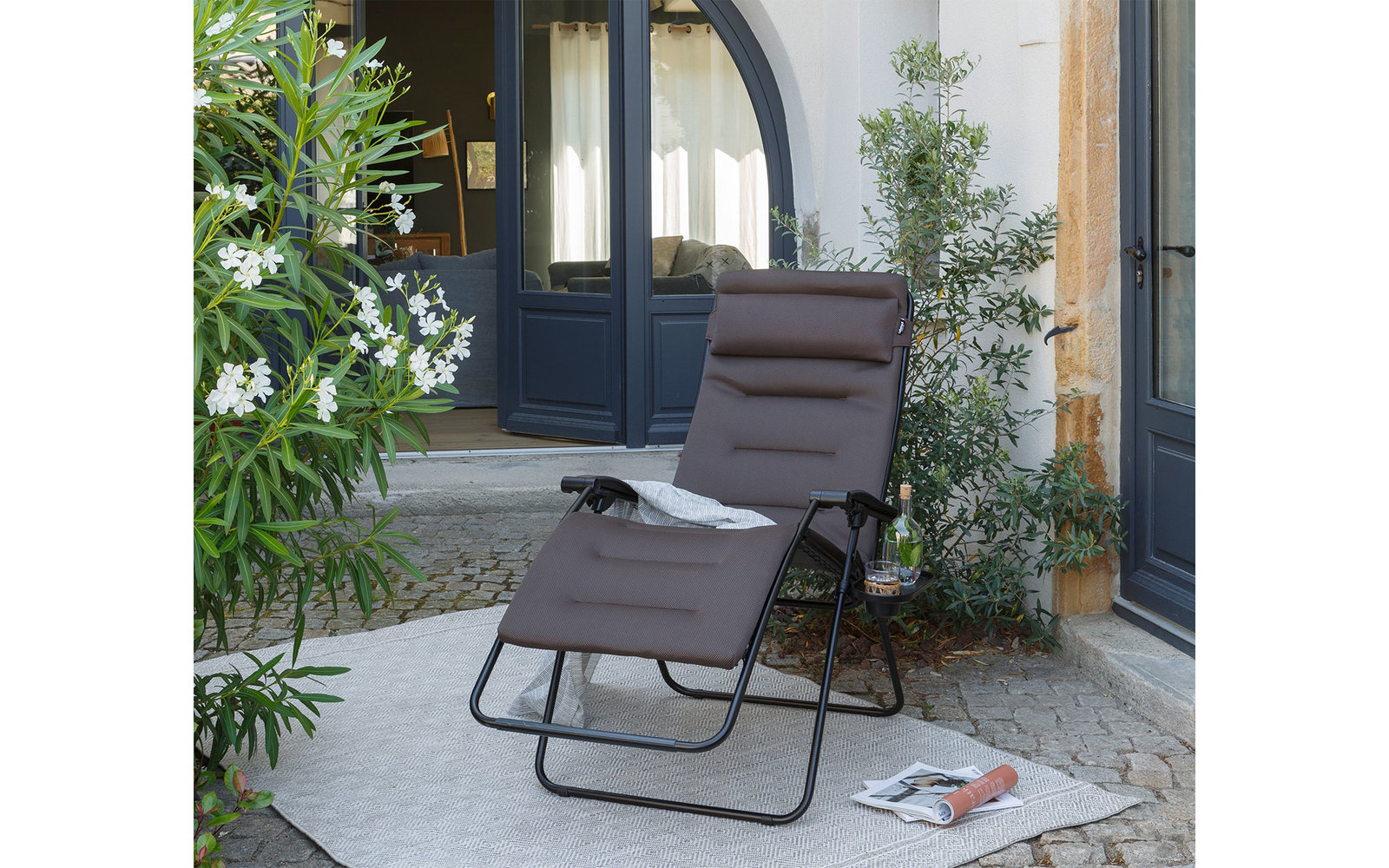 Opvouwbare ligstoel op een terras voor een groot raam met planten