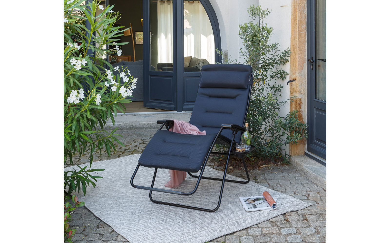 Een moderne buitenstoel met een zwart kussen op een betegeld balkon, omringd door planten