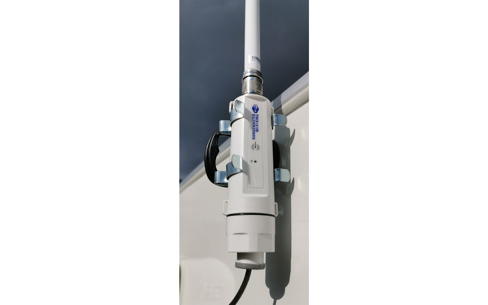 Weißer elektrischer Außenstecker mit Kabel an einer Wand, darüber dunkler Himmel