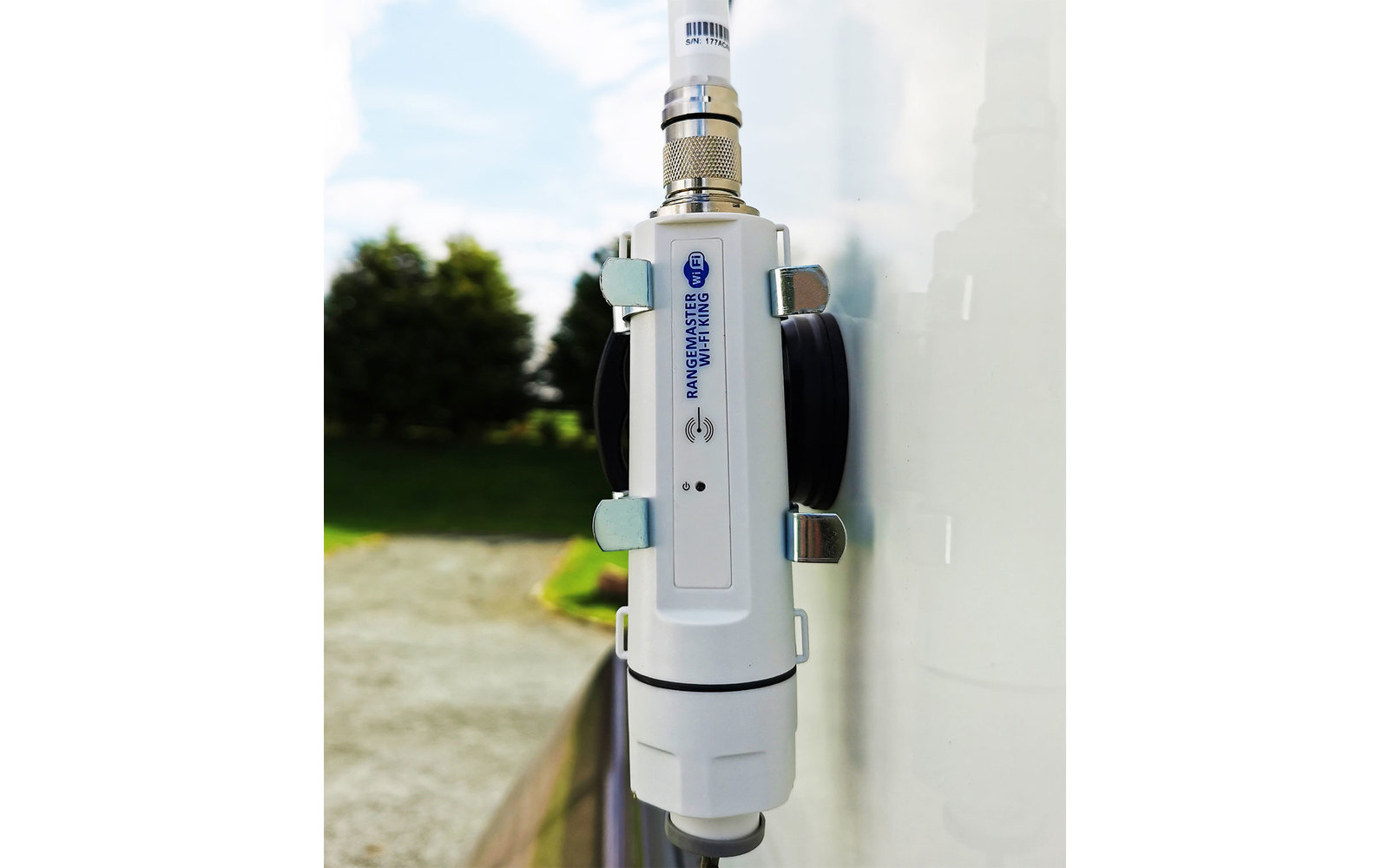 Weißes elektrisches Gerät an einer weißen Wand montiert, im Hintergrund Pflanzen und Himmel