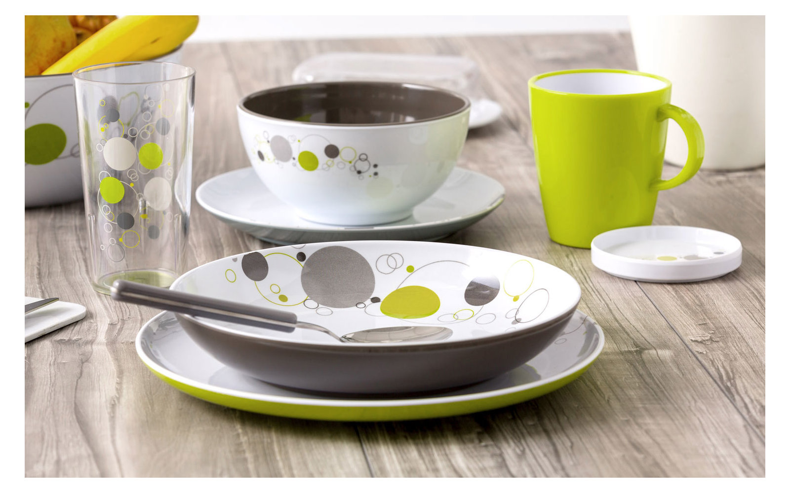 Teller, Schale, Tasse und Glas mit grün-grauen Punkten auf einem Holztisch