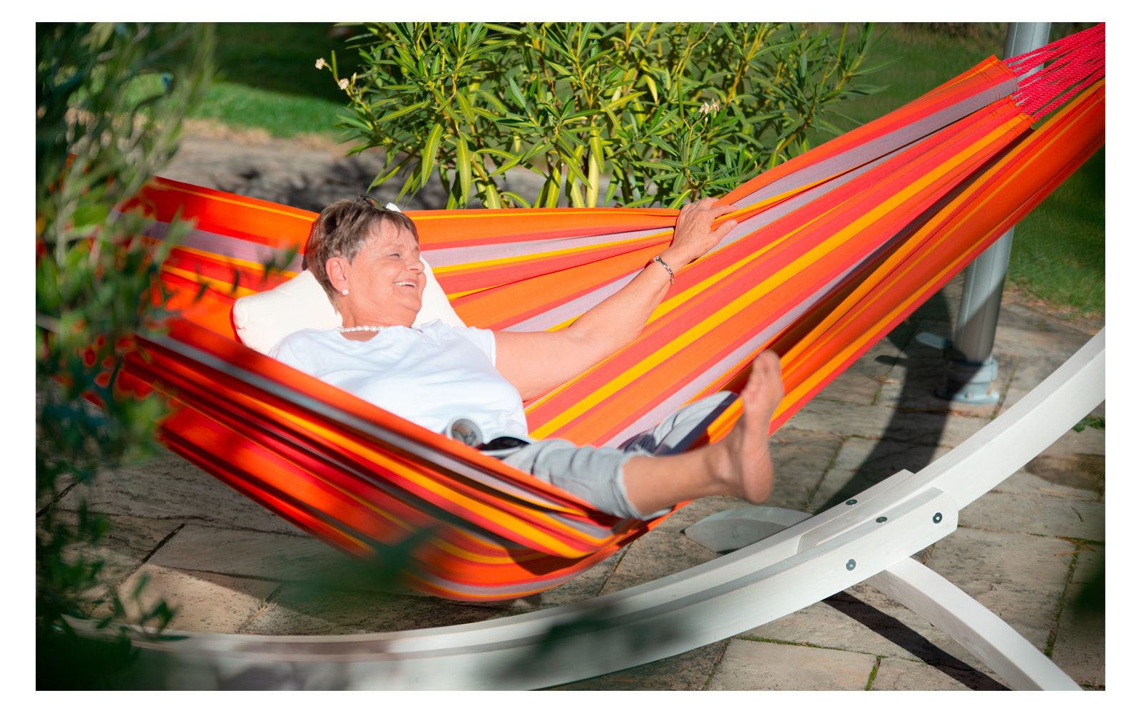 Person liegt in einer bunten Hängematte aus Stoff, auf einem Metallgestell, im Außenbereich