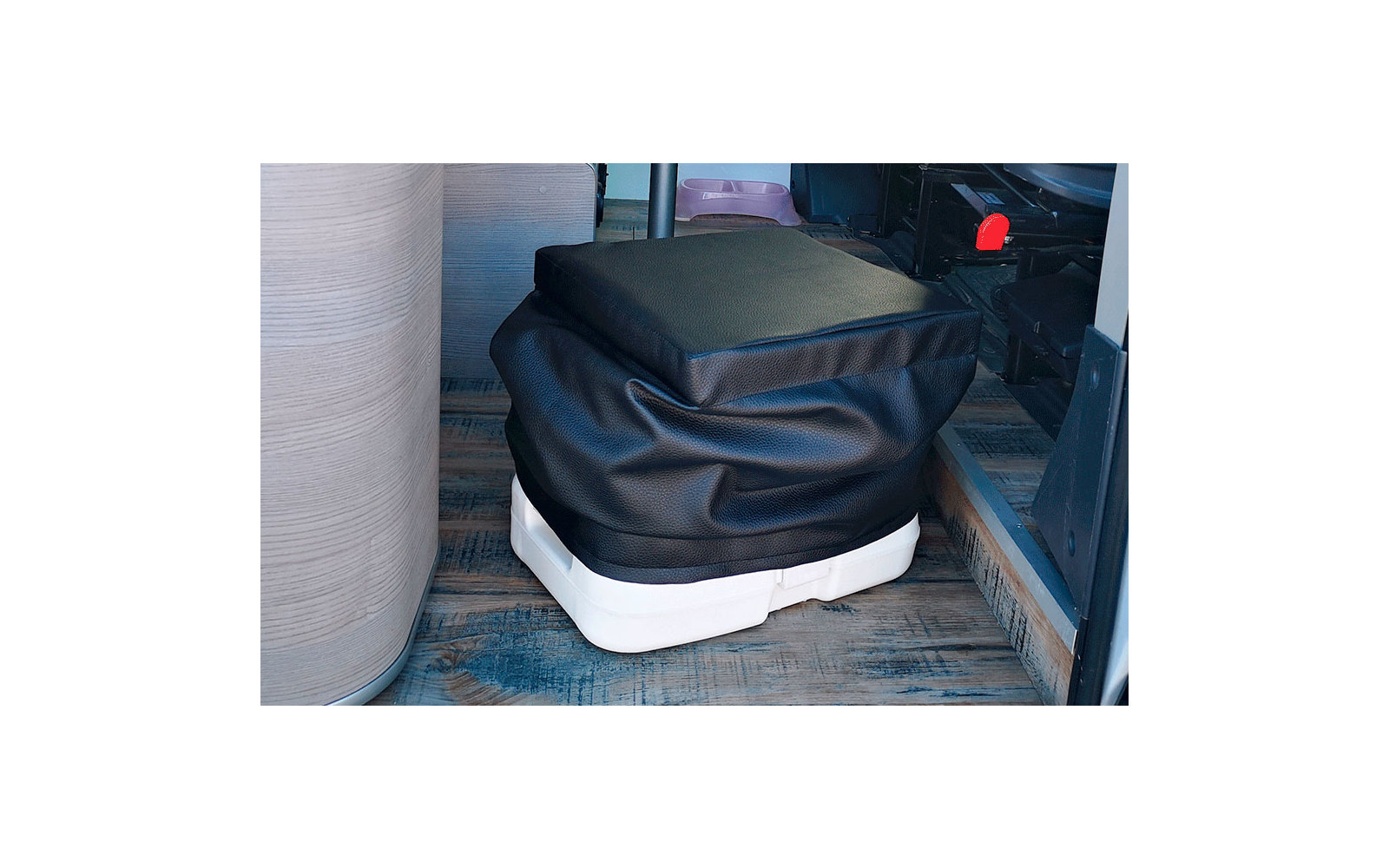 Eine schwarze Sitzgelegenheit mit einem weißen Sockel steht auf einem Holzboden neben einer Glaswand