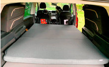 Interior of a vehicle with folded-down back seats and an extended gray camping bed