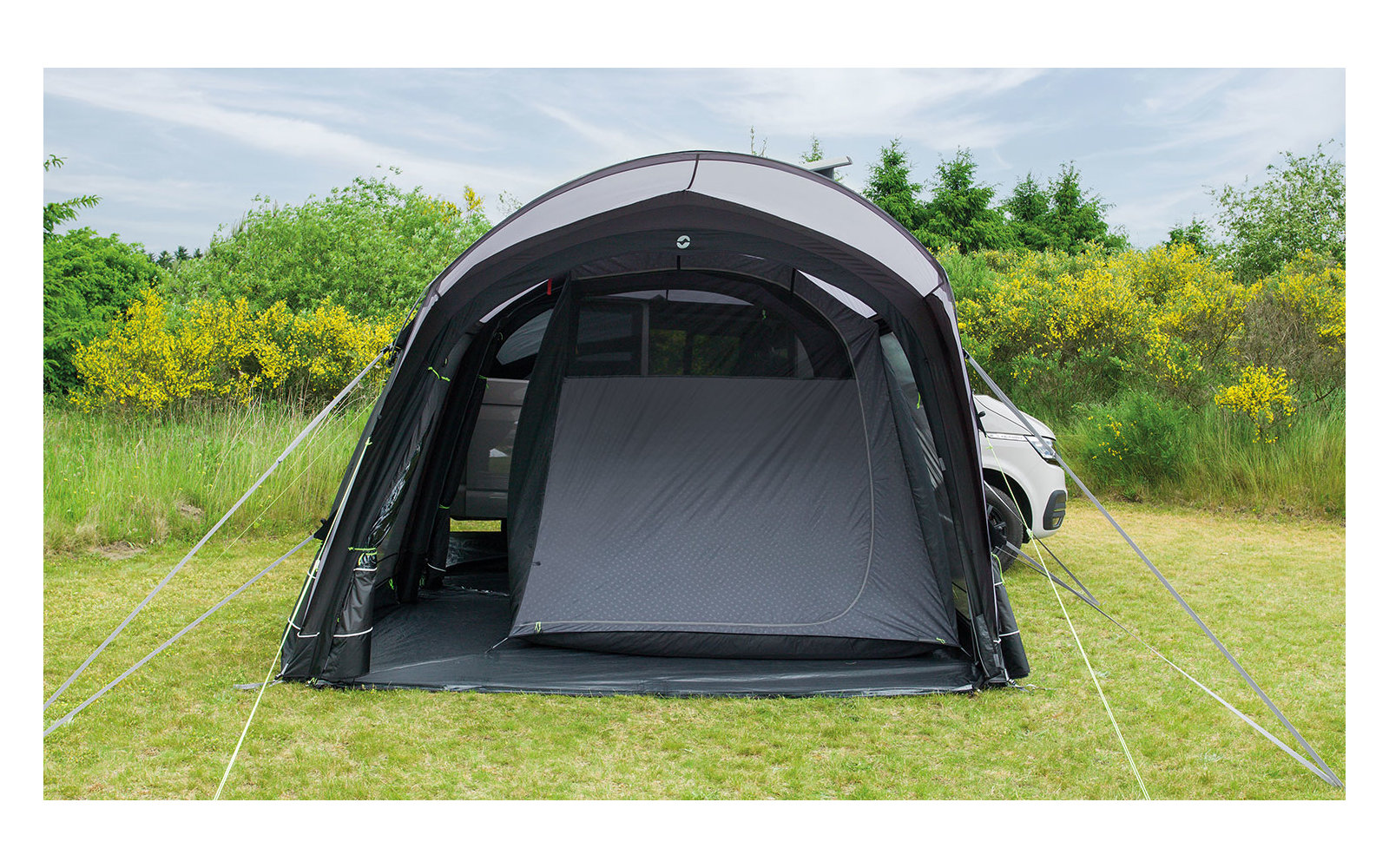 Zelt auf einer grünen Wiese mit Büschen und Bäumen im Hintergrund