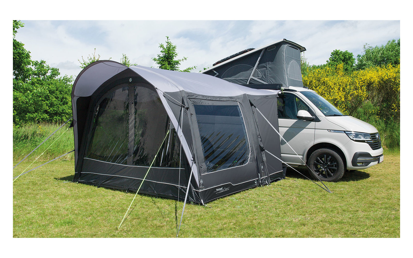 Weißer Campervan mit aufgestelltem Dachzelt und großem grauem Vorzelt auf grünem Gras
