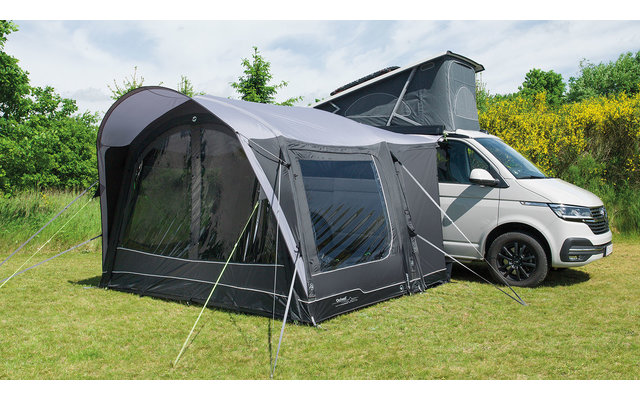 Weißer Campervan mit aufgestelltem Dachzelt und großem grauem Vorzelt auf grünem Gras