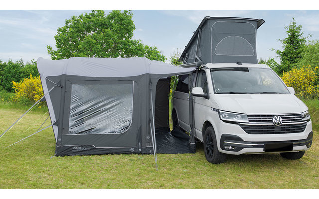 Weißer Van mit aufgestelltem Dachzelt und angebautem grauem Vorzelt auf einer Wiese