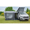 Weißer Van mit aufgestelltem Dachzelt und angebautem grauem Vorzelt auf einer Wiese