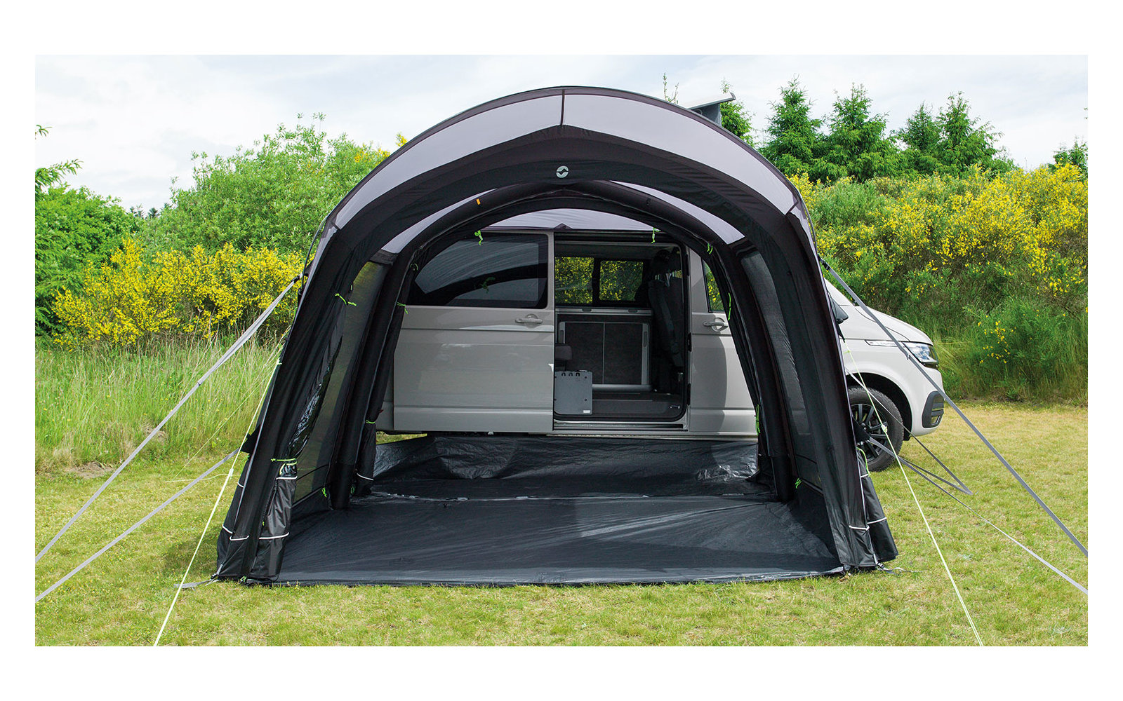 Schwarzes freistehendes Zelt auf einer Wiese, dahinter ein weißes Auto und grüne Bäume