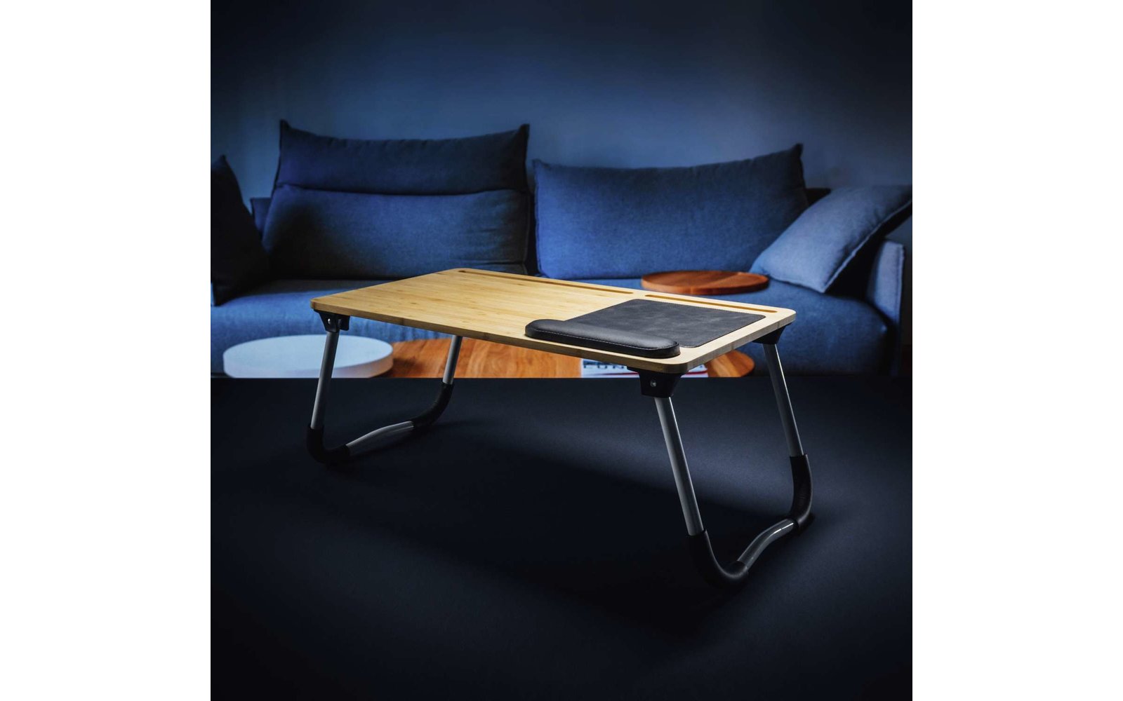 Moderner Holztisch mit Metallbeinen vor einem dunkelblauen Sofa mit zwei Kissen
