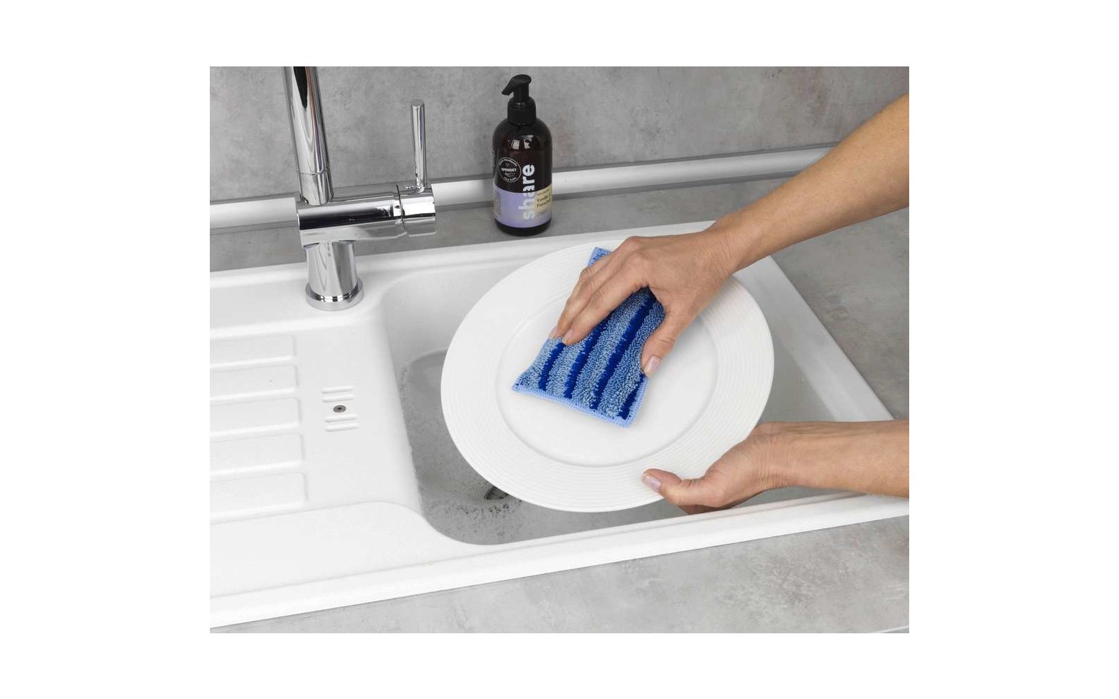 Hände reinigen einen weißen Teller mit einem blauen Schwamm über der Spüle