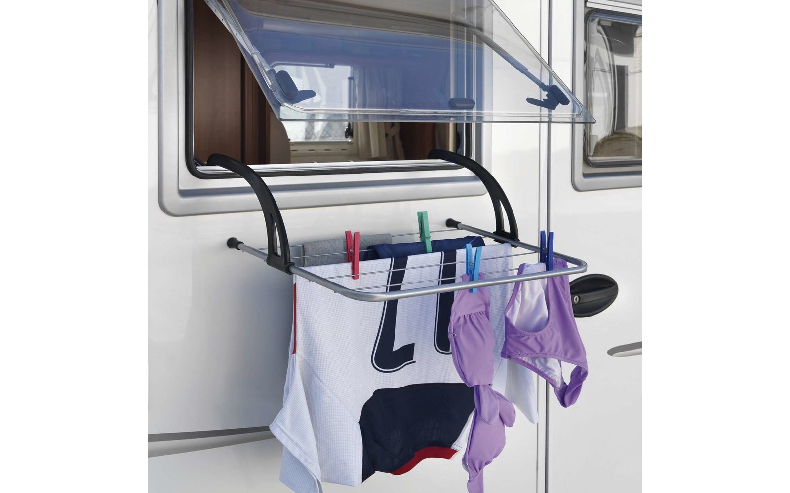 Wäschekorb mit verschiedenen Kleidungsstücken und Käfig an einer Wohnmobilwand