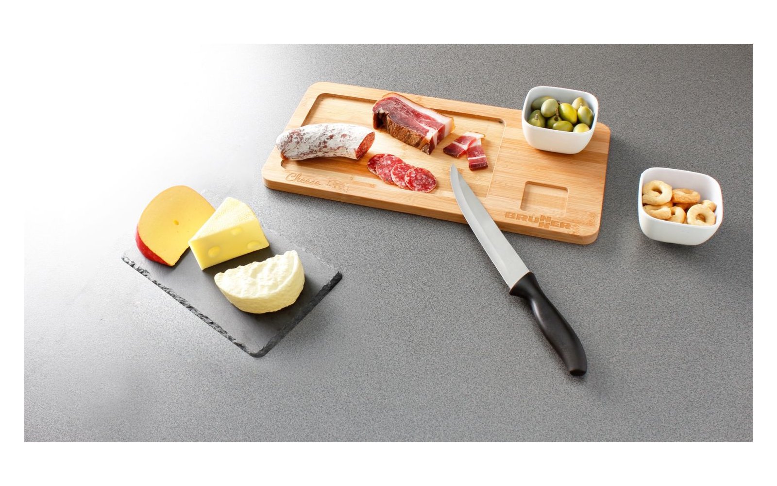 Brett mit verschiedenen Käsesorten, Trauben, Nüssen und Messer auf weißem Untergrund