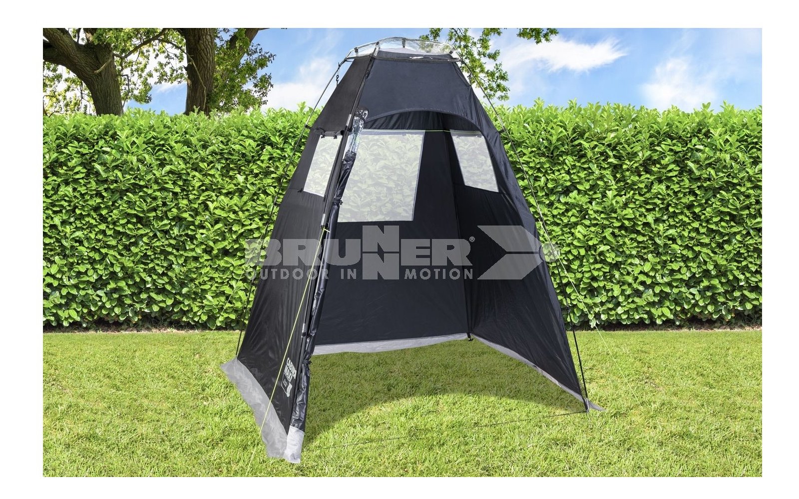 Tenda grigia aperta su erba verde davanti a cespugli verdi