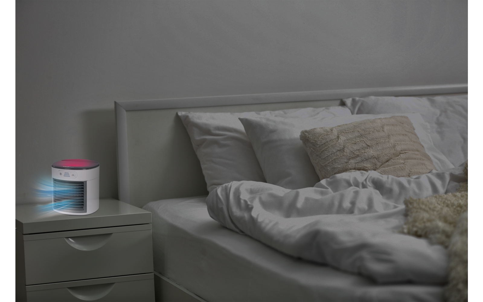Ein ungemachtes Bett mit mehreren Kissen und eine Nachtkommode mit einem leuchtenden Luftbefeuchter