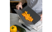 Person schiebt geschnittene orange Paprika von einem Schneidebrett in eine Pfanne