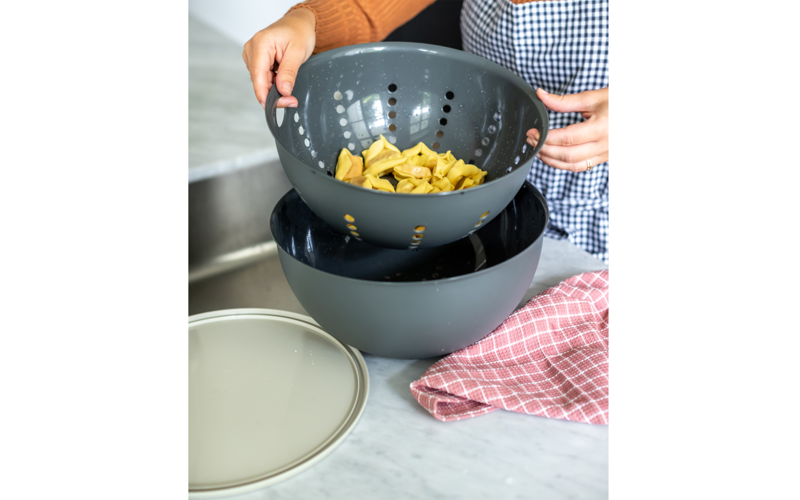 Person gießt Nudeln aus einem Sieb in eine Schüssel