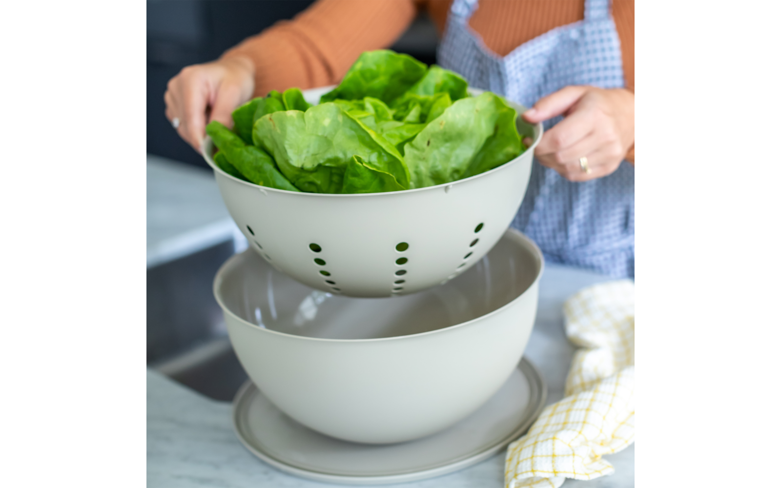 Person hält ein Sieb mit frischem Kopfsalat über einer Schüssel