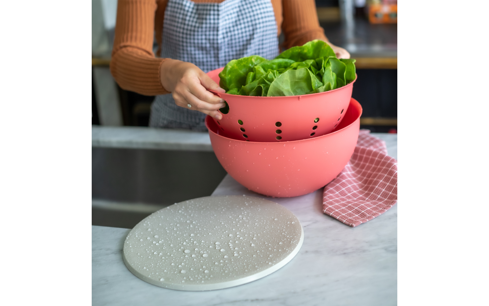 Person hält einen rosa Sieb mit grünem Kopfsalat über der Spüle