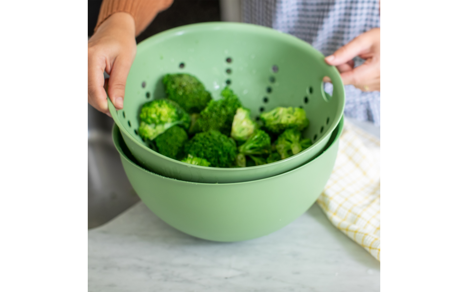 Person wäscht Brokkoli in grünem Küchensieb über Spüle