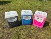 Trois bidons avec des produits de nettoyage en noir, bleu et rose sur l'herbe