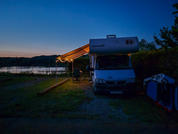 Motorhome parked at a campsite at dusk with a tent and lake in the background