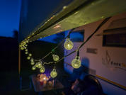 Evening scene at a motorhome with string lights and two people in the foreground