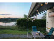 View from a terrace with table and chairs overlooking a lake and forested hills in the background at sunset