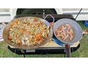 Deux poêles sur une grille de barbecue avec différents plats, dont du riz aux légumes et des crevettes