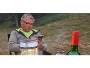 Older man sitting outdoors, looking at a smartphone, table with lamp and bottle in the foreground