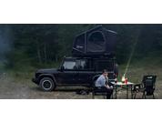 Black car with rooftop tent next to a camping table and two people in the forest