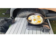 Three fried eggs in a pan on a portable gas stove outdoors