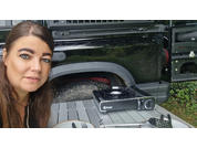 Woman with brown hair next to a black car, camera equipment on the ground