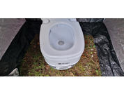 Toilette portative blanche posée au sol, entourée de bâche noire