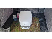 Toilette de camping portable posée sur l'herbe, entourée d'une bâche noire, avec deux récipients à côté