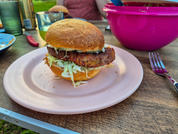 Burger mit Salat und Käse auf einem rosa Teller, daneben ein pinker Drink im Glas