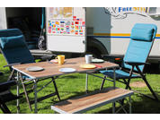 Een tuintafel met twee blauwe stoelen en een bankje op groen gras voor een wit gebouw