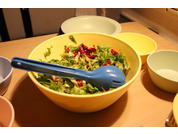 Eine Schüssel mit Salat und einem Löffel, daneben leere weiße Schüsseln auf einem Holztisch