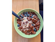 Grüne Schüssel mit Milch, runden Schokoladenflocken, Blaubeeren und einem Löffel auf einem Holztisch