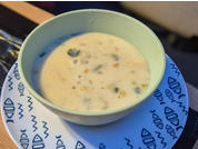 Grüne Schüssel mit heller, cremiger Suppe mit kleinen Stücken, auf weißem Teller mit blauem Muster