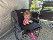 Small child sitting in a black high chair, holding a toy, window and other furniture in the background