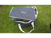 Geöffnete dunkelgraue Stofftasche mit weißen Tragegriffen auf Gras, darin eine Ananas und bunte Gegenstände, Deckel teilweise offen mit Schriftzug 'Berger'