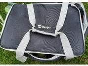 Schwarze Tasche mit hellgrauen Tragegriffen und Schriftzug "Berger", teilweise geöffnet, grüne Stangen sichtbar, liegt auf Gras
