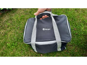 Hand hält Griff einer schwarzen Stofftasche mit grauen Tragegriffen und weißem Berger-Logo; Tasche auf Gras